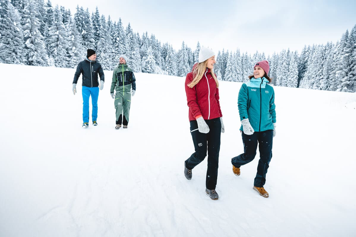 Zwei Paare beim Winterspaziergang vor verschneiten Bäumen